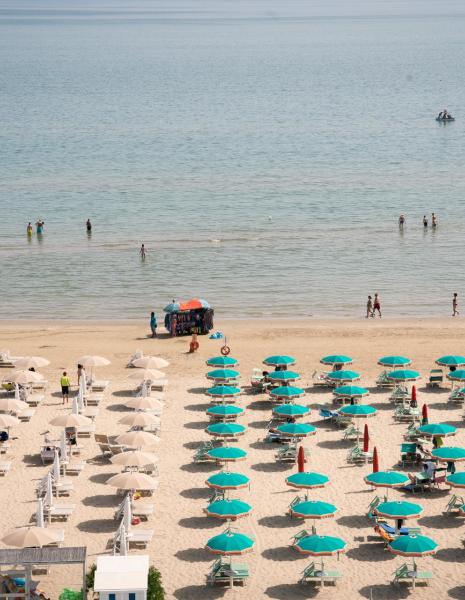 Spiaggia con ombrelloni colorati e persone in acqua.