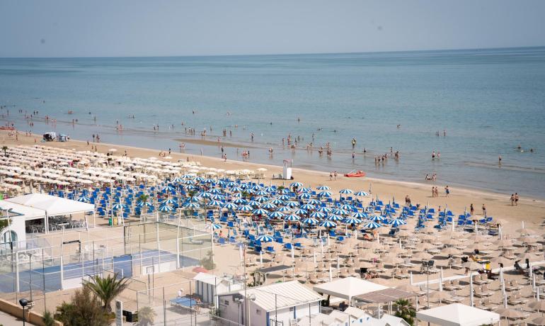 Spiaggia affollata con ombrelloni colorati e persone che nuotano nel mare.