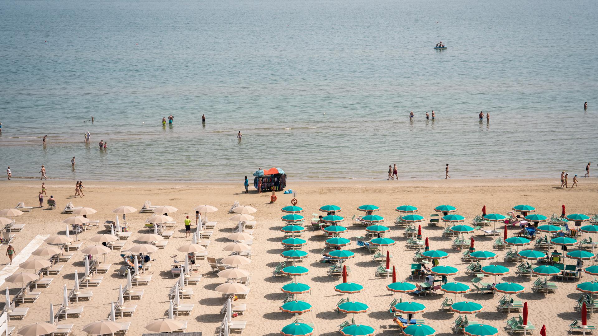Crowded beach with colorful umbrellas and swimmers in the sea.