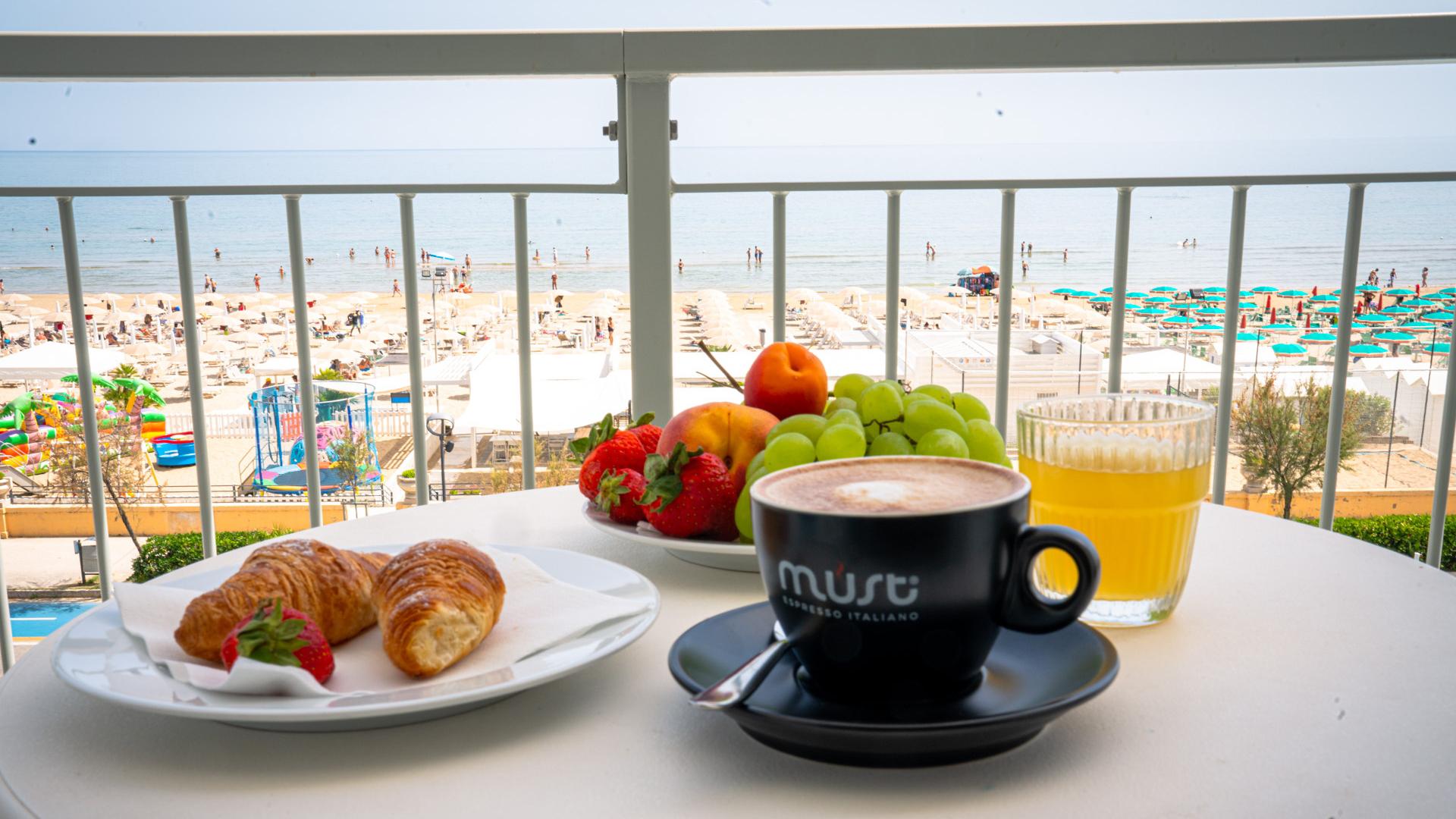 Breakfast with sea view: fruit, croissants, coffee, and juice.