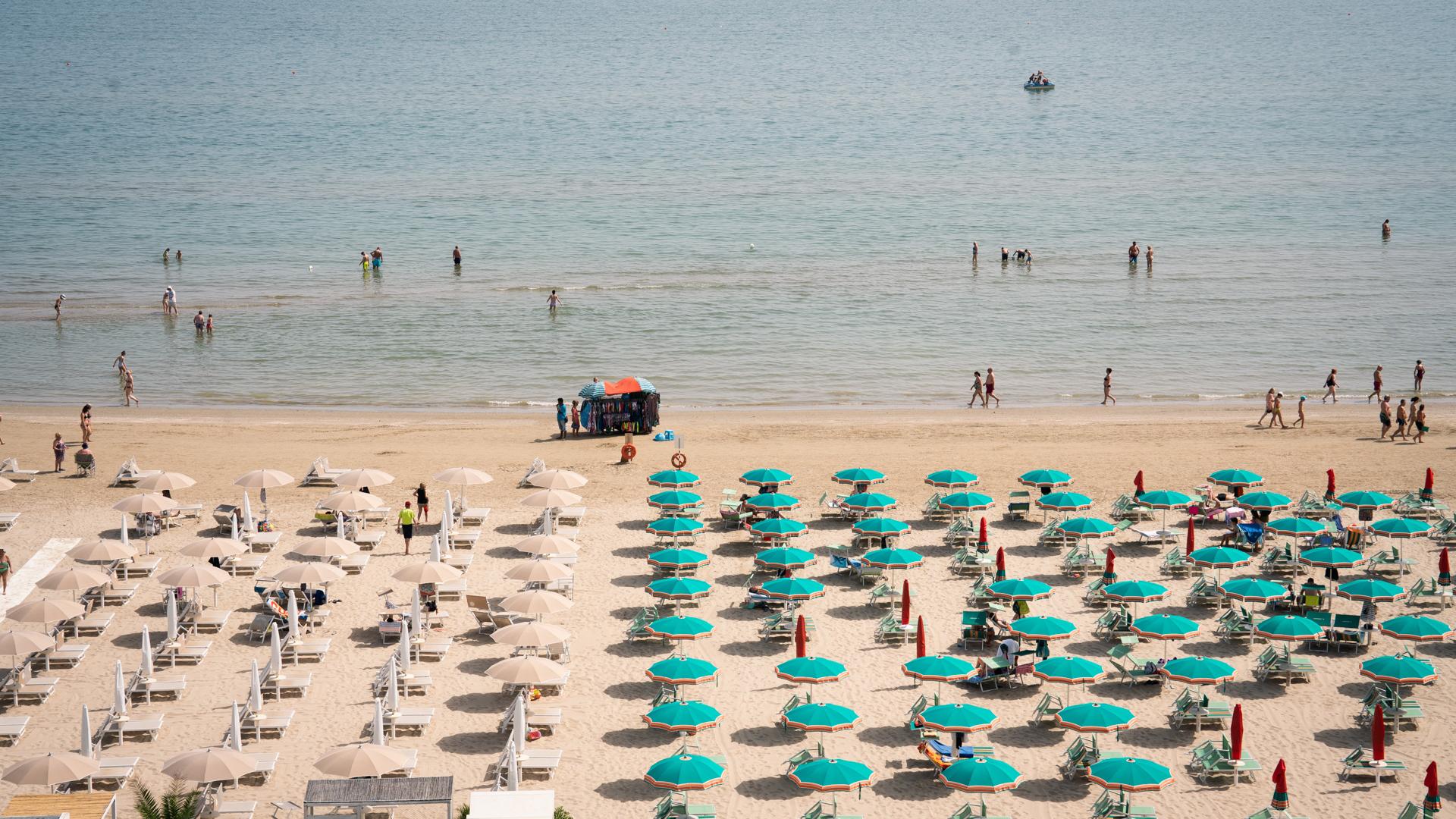 Plage avec des parasols colorés et des baigneurs dans la mer.