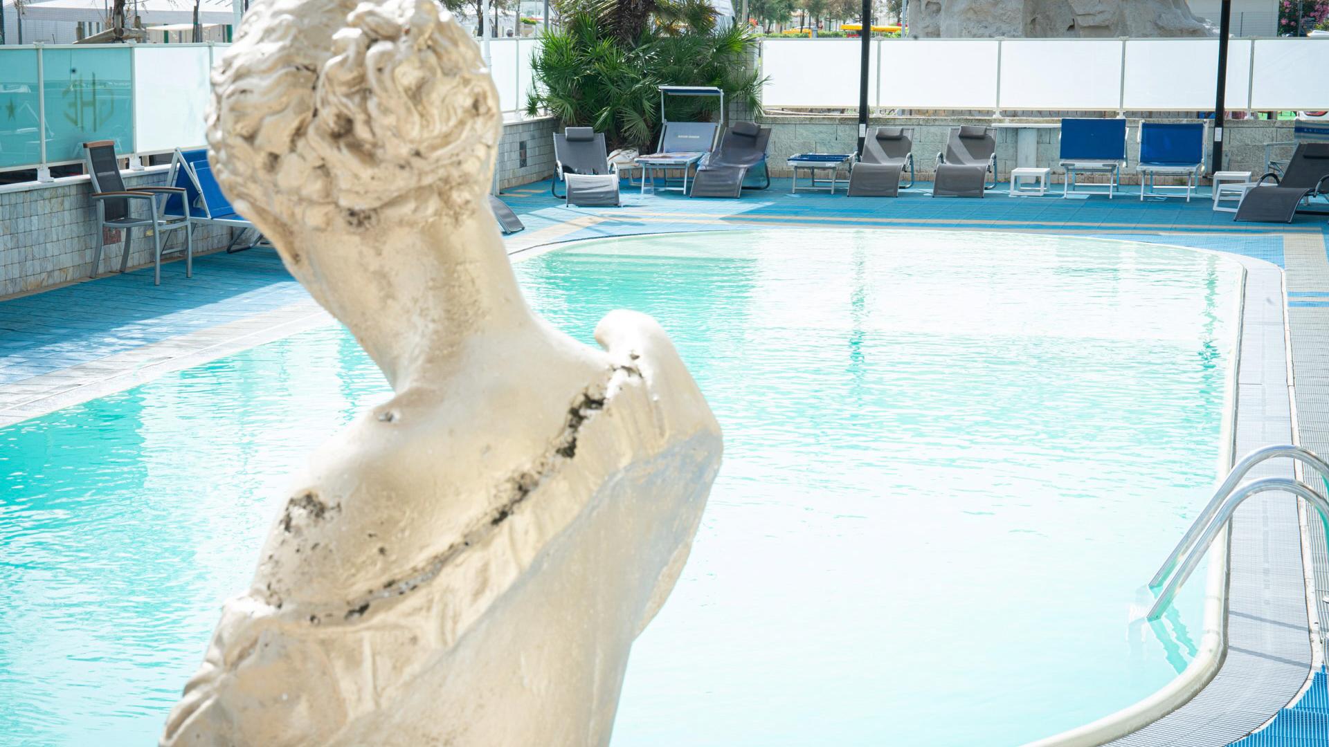 Statue beside a pool with loungers and chairs.