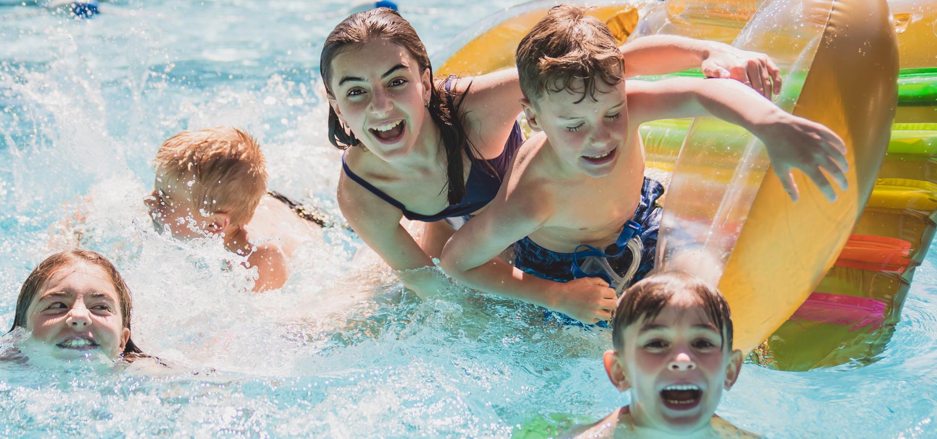 Bambini giocano felici in piscina con materassino.