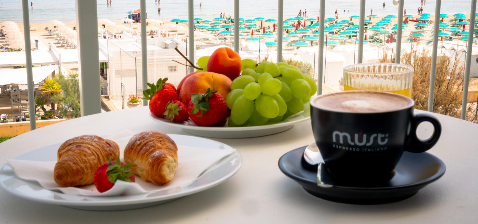 Colazione vista mare con frutta, croissant e cappuccino.