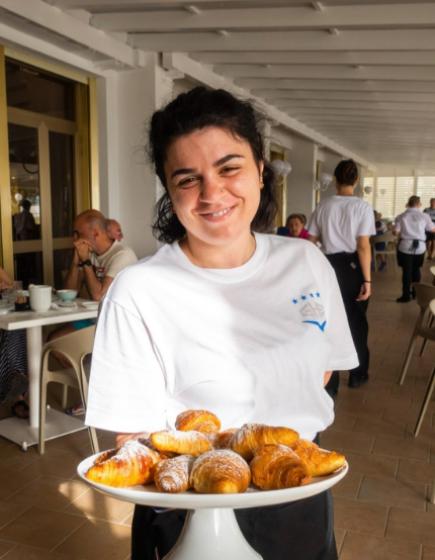 Cameriera sorridente con vassoio di croissant in un ristorante.