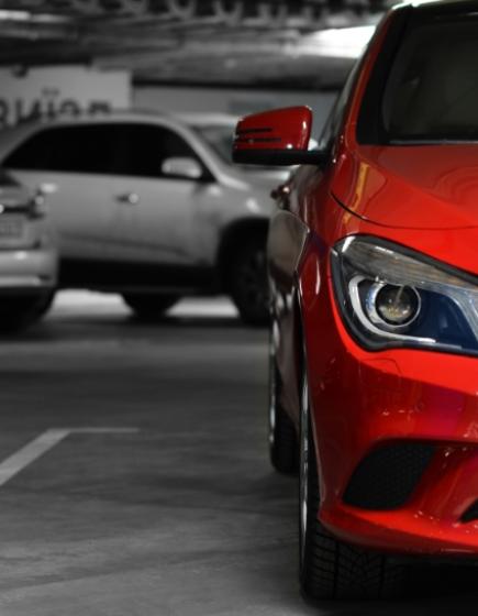 Red car in a parking lot, other cars in black and white background.