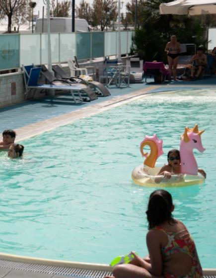 Pool with people and colorful inflatables under the sun.