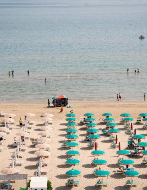 Spiaggia affollata con ombrelloni colorati e bagnanti nel mare.