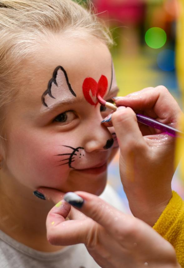 Bambina con pittura facciale da gatto, cuore rosso sulla fronte.