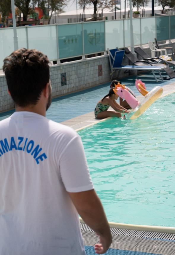 Bambina gioca in piscina con salvagente, uomo osserva.