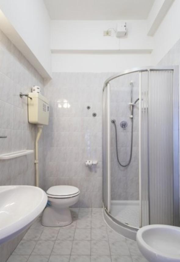 Bagno con doccia, WC, lavabo e bidet, piastrelle bianche.