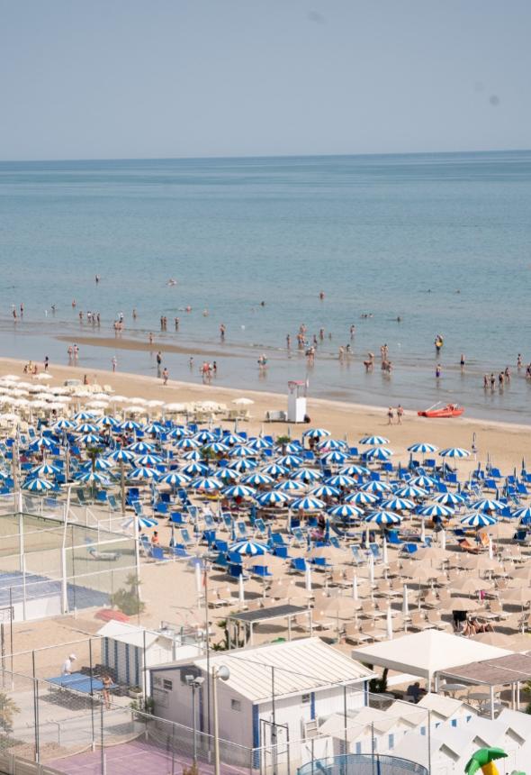 Crowded beach with blue and white umbrellas, calm sea.