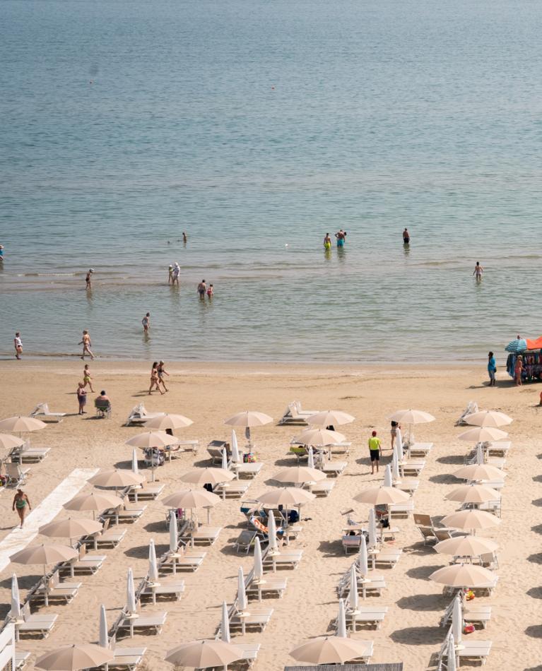 Crowded beach with colorful umbrellas and swimmers in the sea.